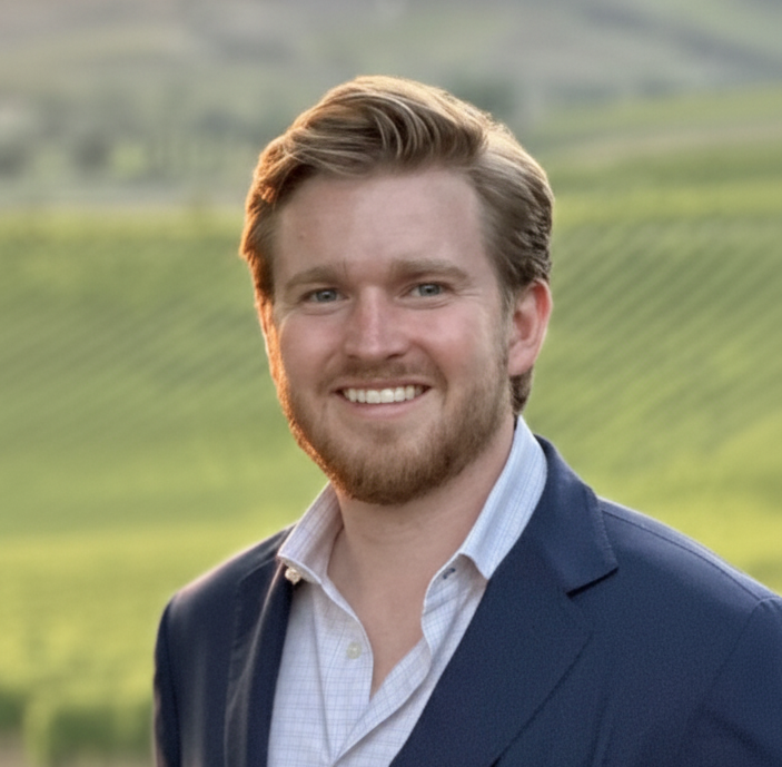 Nicholas Rinard, photographed outdoors at a vineyard in golden light, wearing a navy blazer